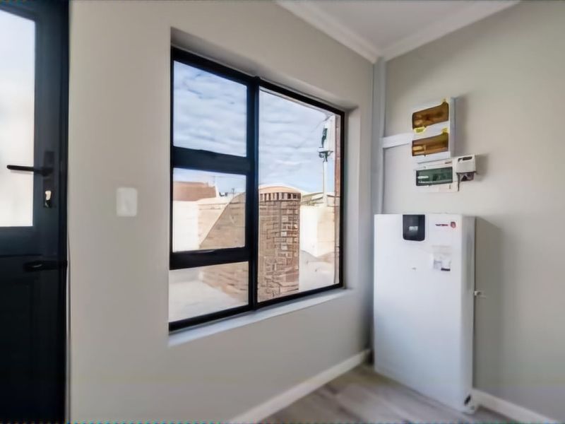 A clean utility space featuring an installed inverter system, electrical distribution board, modern laminate flooring, and an external door with aluminium window frames.