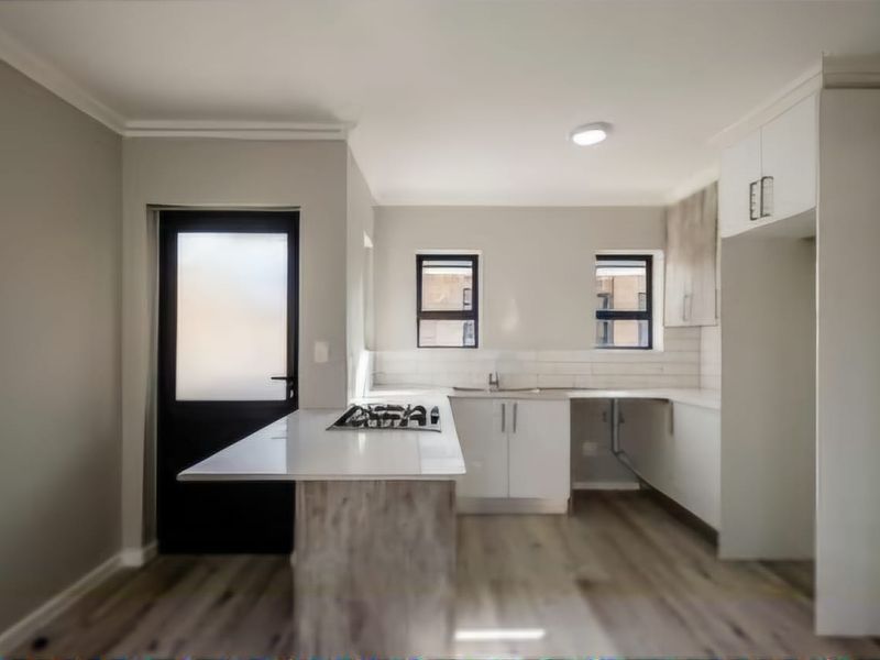 Modern kitchen featuring a central island with a gas hob, white cabinetry, subway tile backsplash, and durable laminate flooring with direct exterior access.