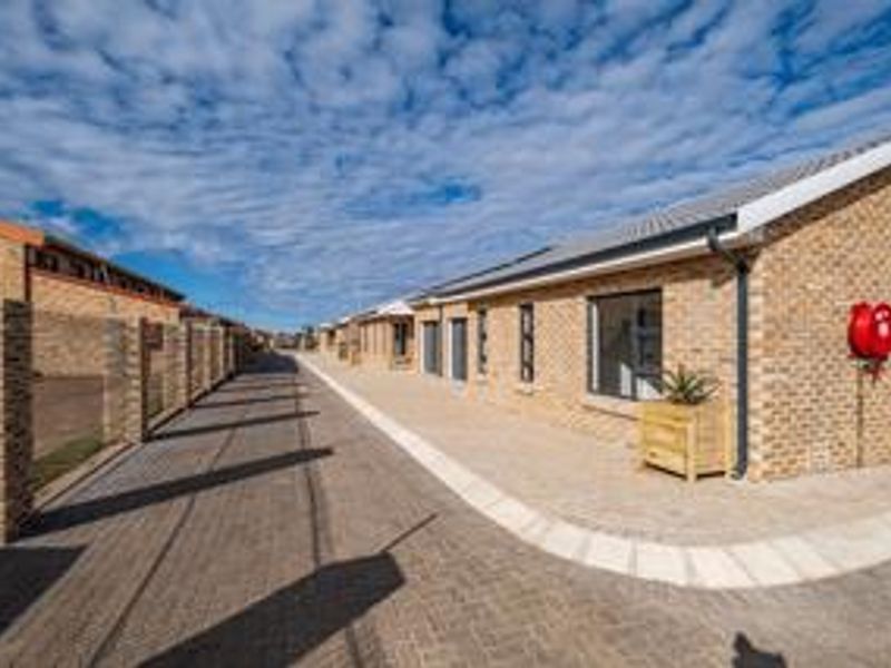A well-maintained townhouse exterior featuring a face brick facade, paved driveway, and modern aluminium window frames within a secure complex setting.