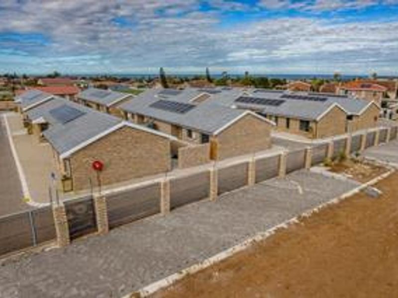 Aerial view of a townhouse complex featuring brick construction, tiled roofs with solar panels, and secure perimeter fencing with paved access.