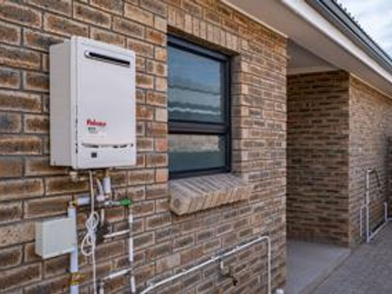 Exterior view of the townhouse rear facade featuring a wall-mounted gas geyser, brickwork, and paved walkway.