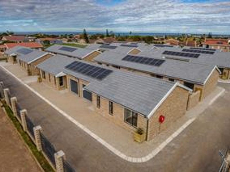 Aerial view of a modern townhouse complex featuring brick exteriors, tiled roofs, integrated solar panels, and paved access roads.