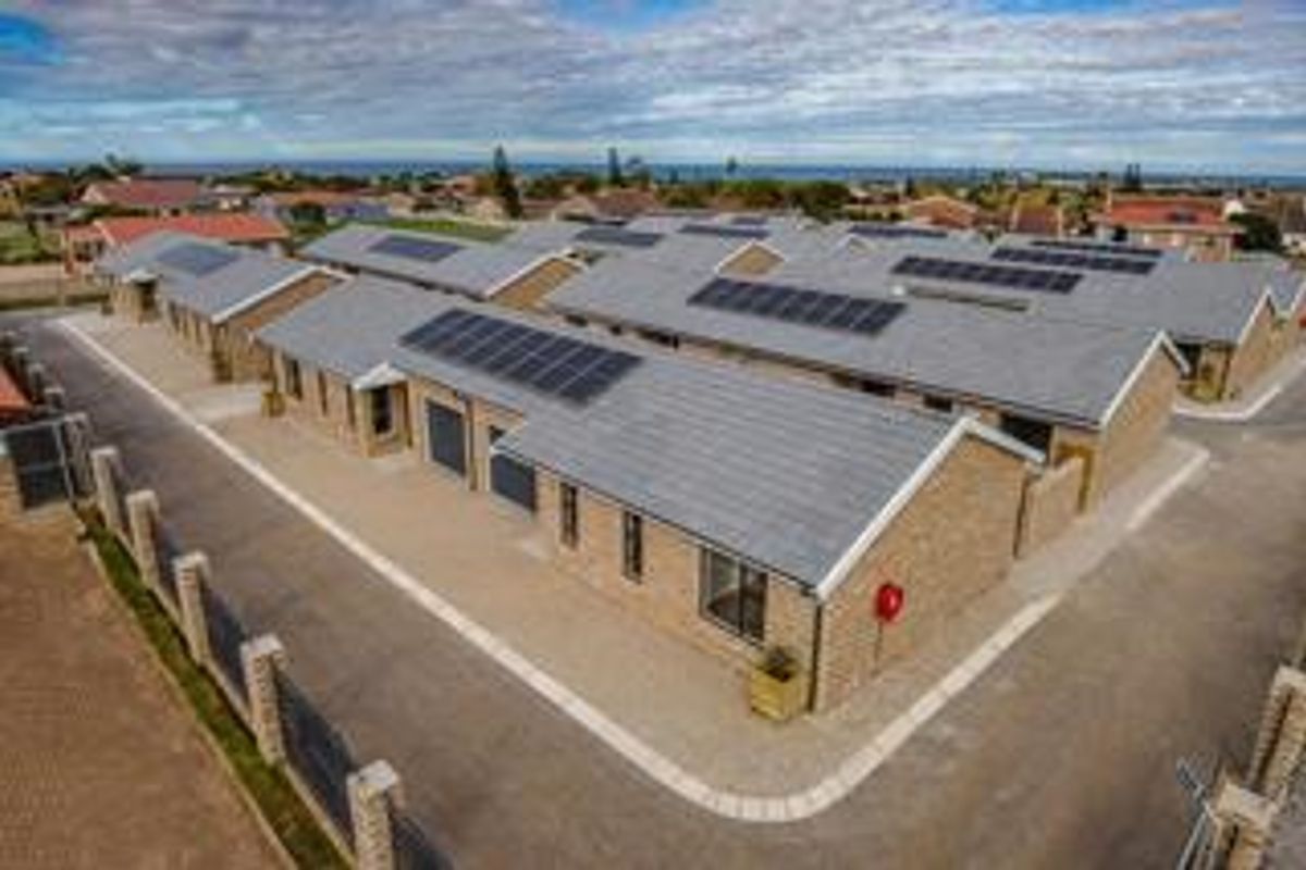 Aerial view of a modern townhouse complex featuring brick exteriors, tiled roofs, integrated solar panels, and paved access roads.