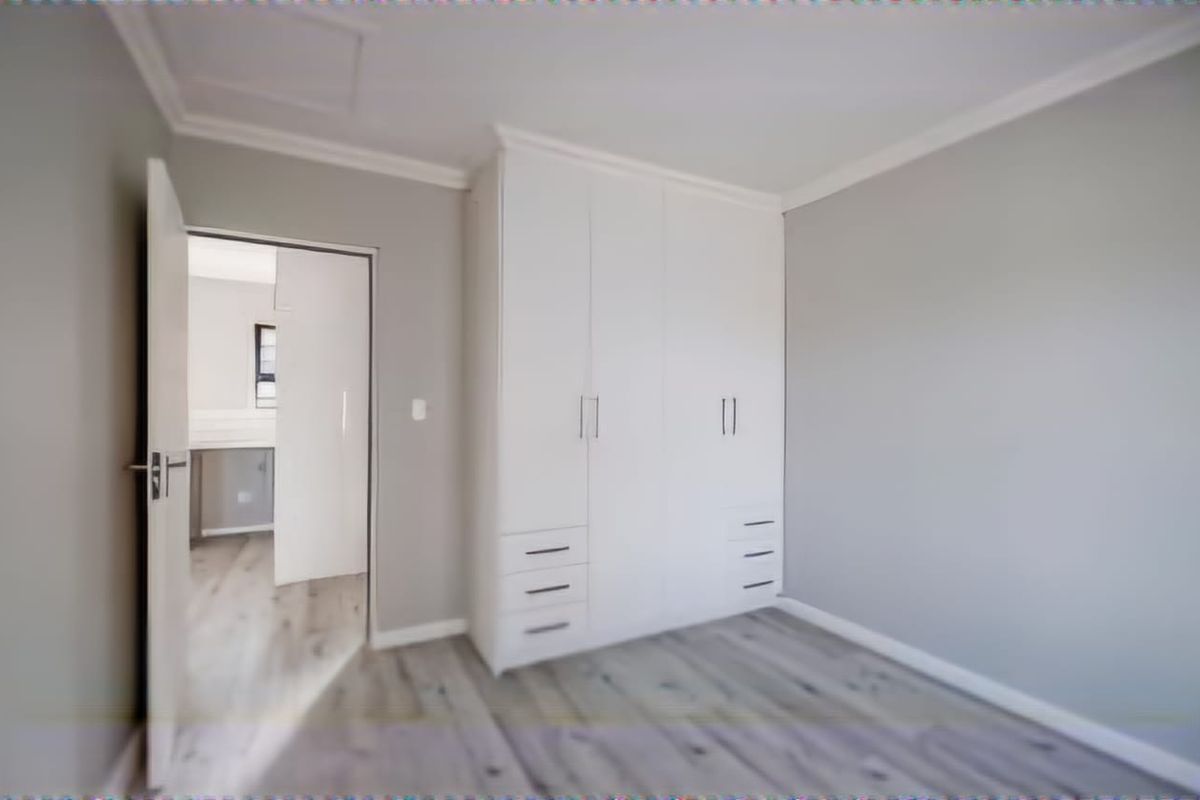 A clean, empty bedroom featuring modern white built-in cupboards, light grey walls, and durable laminate flooring, offering a neutral canvas for personalization.