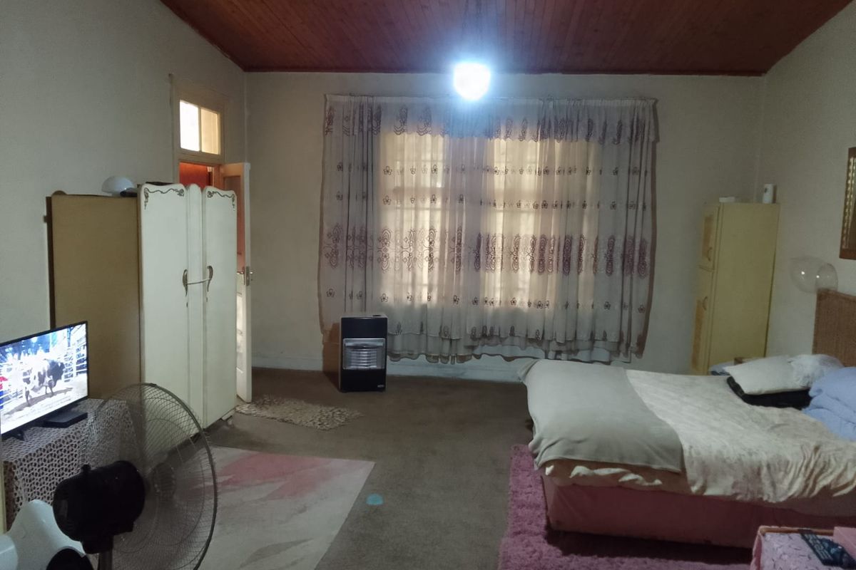 A spacious bedroom featuring a timber ceiling and carpeted flooring, offering a dated aesthetic with potential for modernization.