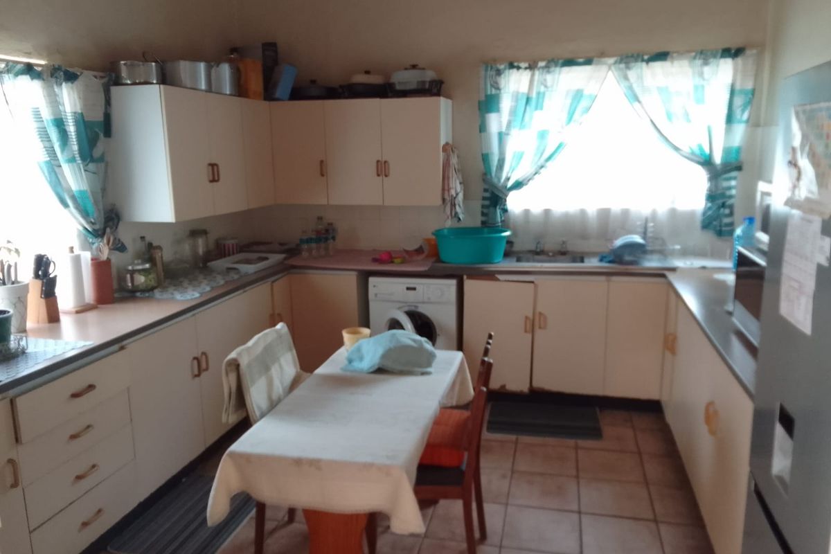 A functional kitchen featuring laminate countertops, built-in cabinetry, tiled flooring, and an integrated washing machine, offering potential for a modern renovation.