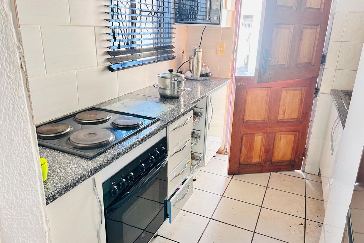 Compact kitchen featuring granite countertops, built-in oven, electric hob, and tiled flooring with direct access to the exterior.