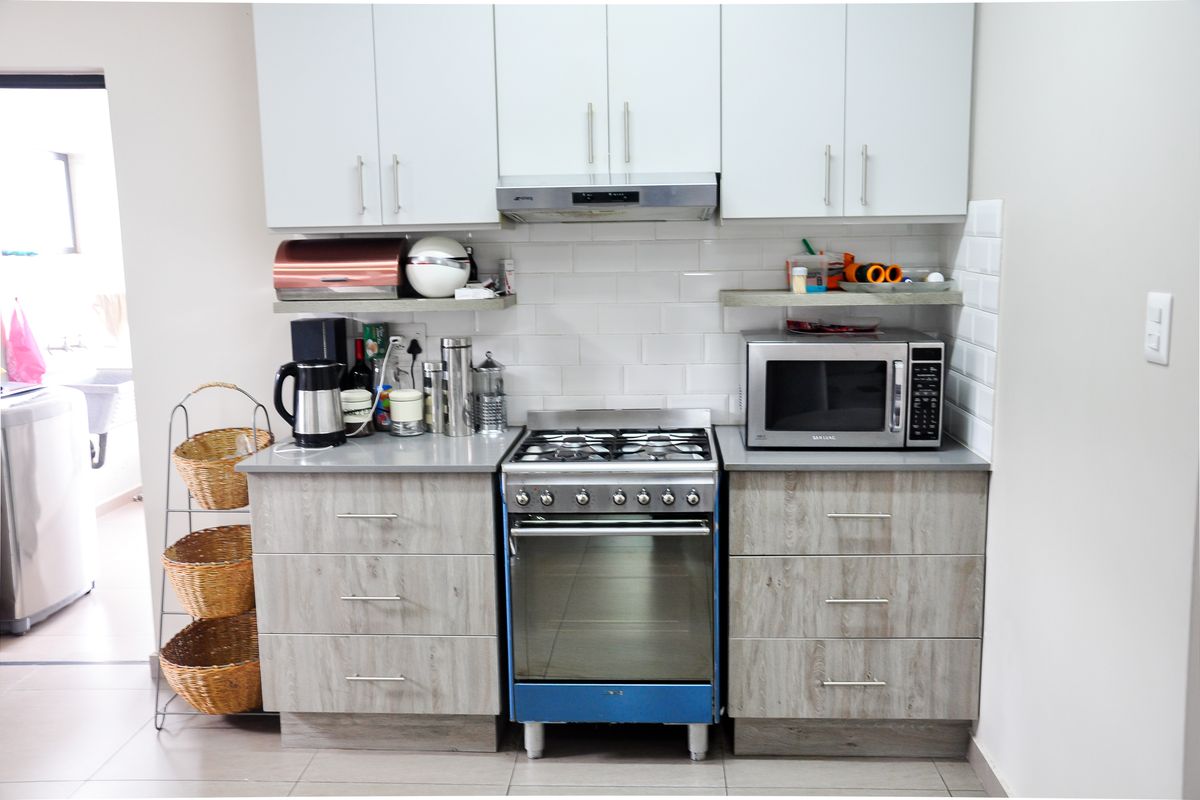 Compact kitchen featuring modern wood-grain cabinetry, white subway tile backsplash, stainless steel gas stove, and built-in extractor fan.