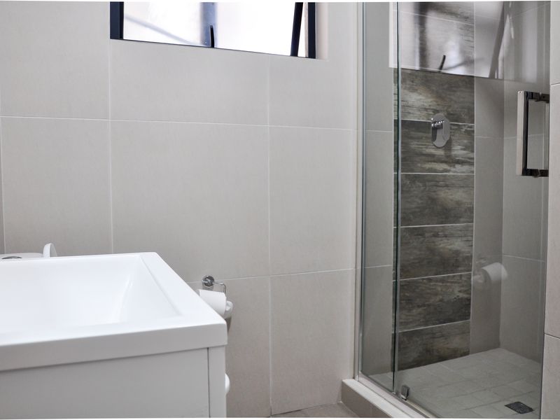 Modern bathroom featuring a glass-enclosed shower with wood-look tile accents, a contemporary vanity, and neutral wall tiling.