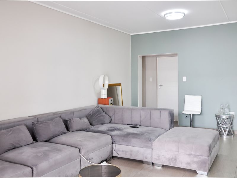 A well-maintained living room featuring neutral wall tones, tiled flooring, and a clean, modern layout with access to an adjacent room.