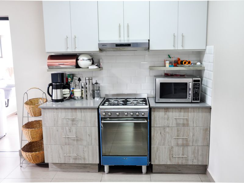 Compact kitchen featuring modern wood-grain cabinetry, white subway tile backsplash, stainless steel gas stove, and built-in extractor fan.