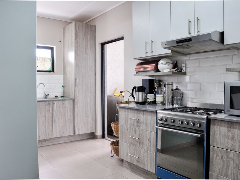 Modern kitchen featuring light wood-grain cabinetry, subway tile backsplash, stainless steel gas stove with extractor fan, and tiled flooring with access to a laundry area.