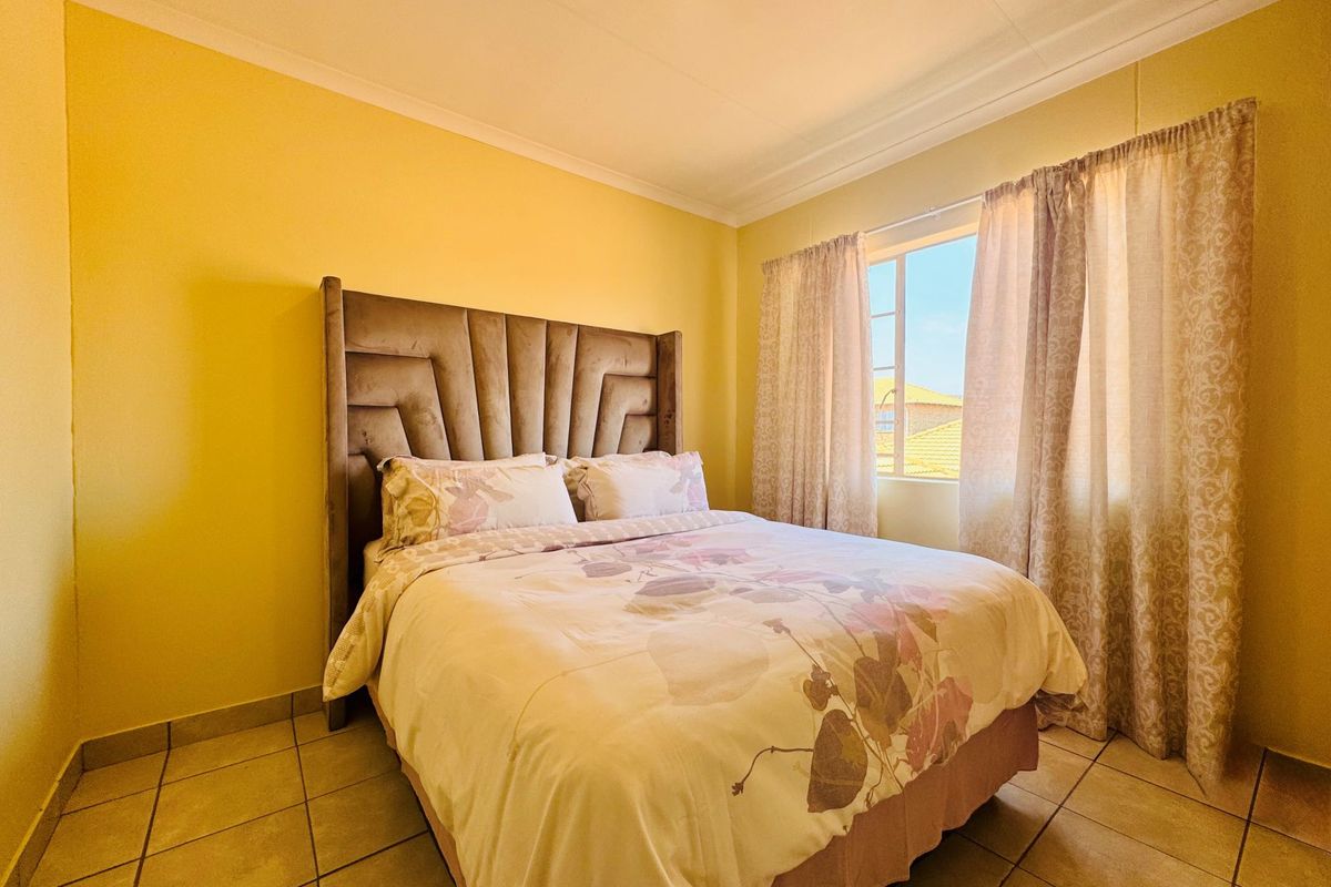 A bedroom featuring tiled flooring and a window with curtains, providing natural light and a view of the surrounding area.