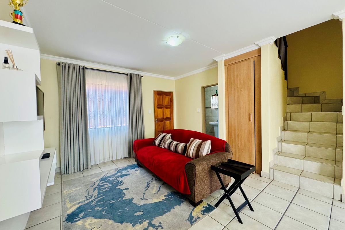 A living room featuring tiled flooring, a built-in storage cupboard, and an adjacent staircase leading to the upper level.