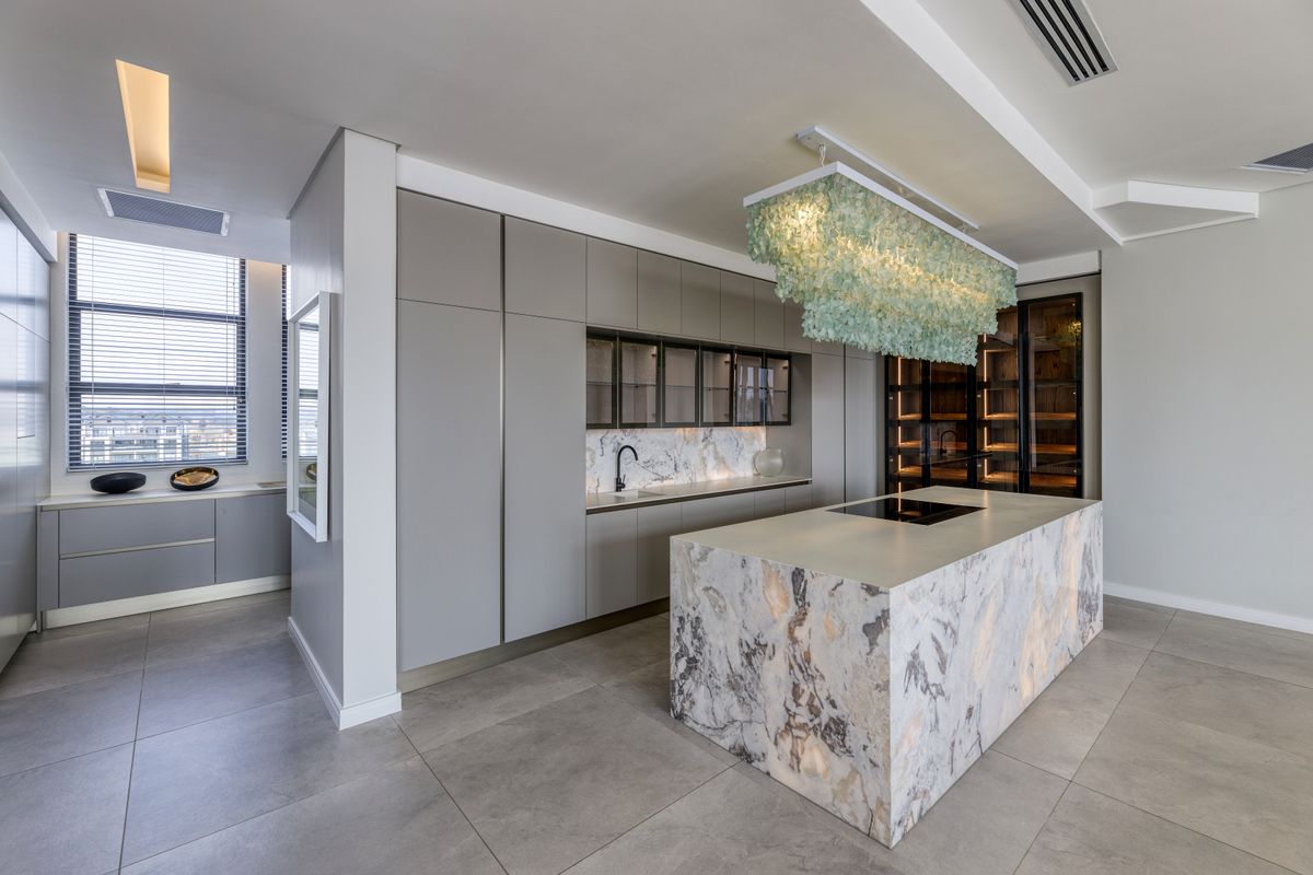 Modern luxury kitchen featuring a large marble-clad island with integrated cooktop, sleek handleless cabinetry, and high-end finishes in an open-plan penthouse setting.
