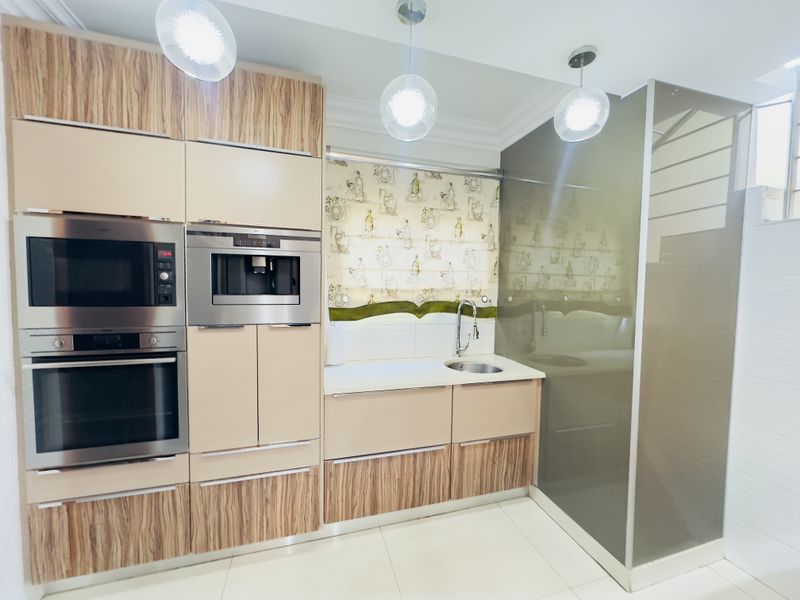 Modern kitchen featuring integrated appliances, including an oven, microwave, and coffee machine, with sleek cabinetry and contemporary pendant lighting.