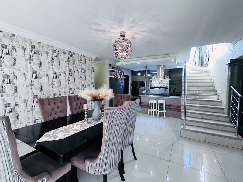 Open-plan living and dining area featuring polished floor tiles, a modern staircase with glass balustrades, and a contemporary kitchen with integrated cabinetry.