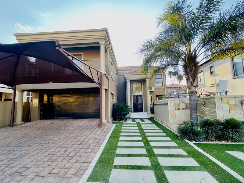Front elevation of a modern house featuring a paved driveway with shade sail, double garage, and a landscaped walkway leading to the entrance.