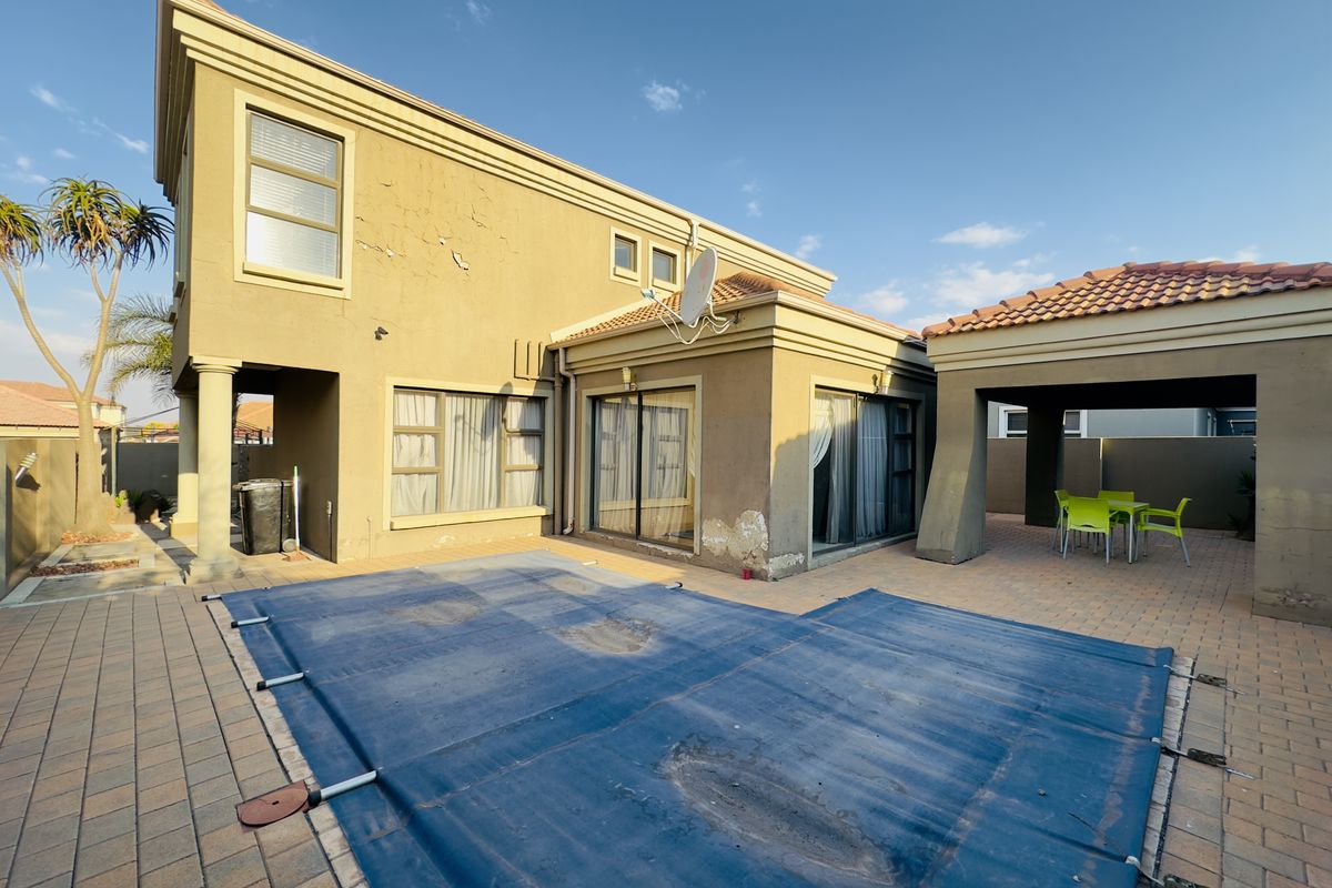 Rear exterior view of the house featuring a paved patio area, a covered outdoor space, and a swimming pool with a cover.