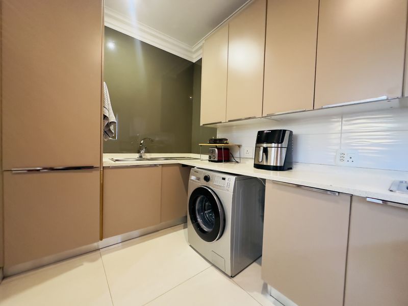A modern, well-maintained laundry area featuring sleek built-in cabinetry, stone countertops, a stainless steel sink, and tiled finishes.
