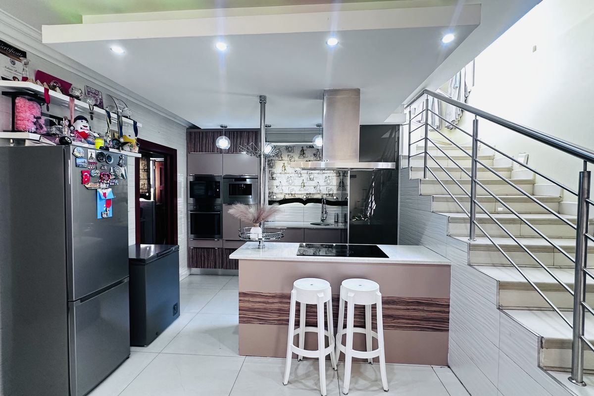 Modern kitchen featuring a central island with integrated hob, built-in appliances, sleek cabinetry, and an adjacent staircase with stainless steel railings.
