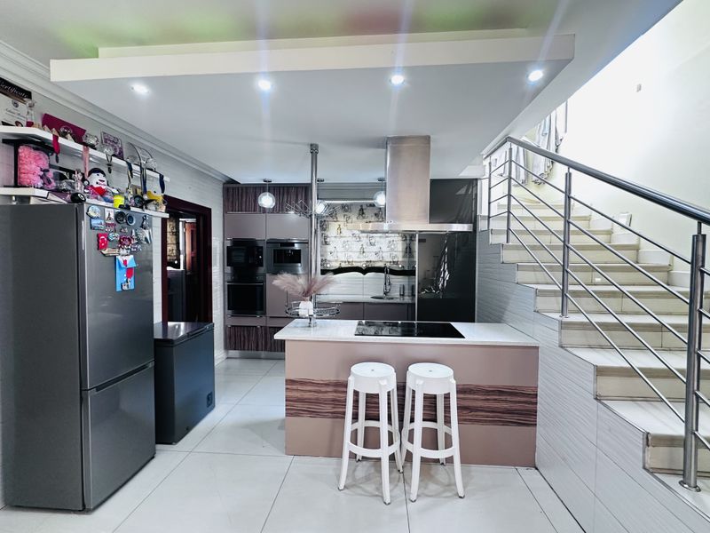 Modern kitchen featuring a central island with integrated hob, built-in appliances, sleek cabinetry, and an adjacent staircase with stainless steel railings.