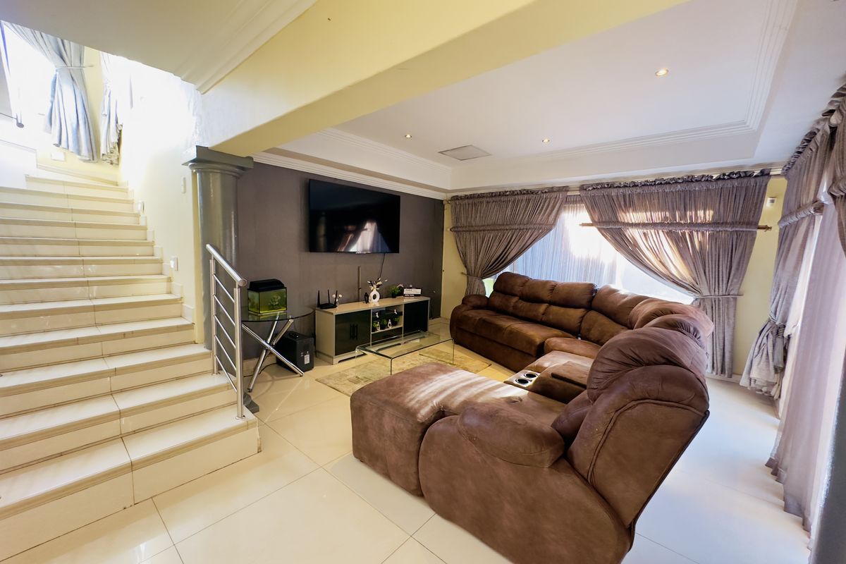 Spacious living room featuring tiled flooring, a modern staircase with stainless steel balustrade, and recessed ceiling lighting, creating an open and inviting atmosphere.