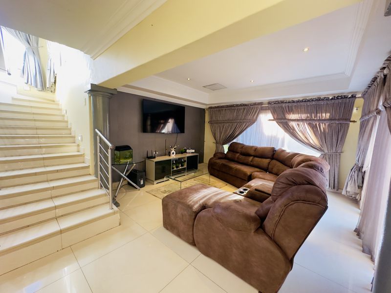 Spacious living room featuring tiled flooring, a modern staircase with stainless steel balustrade, and recessed ceiling lighting, creating an open and inviting atmosphere.
