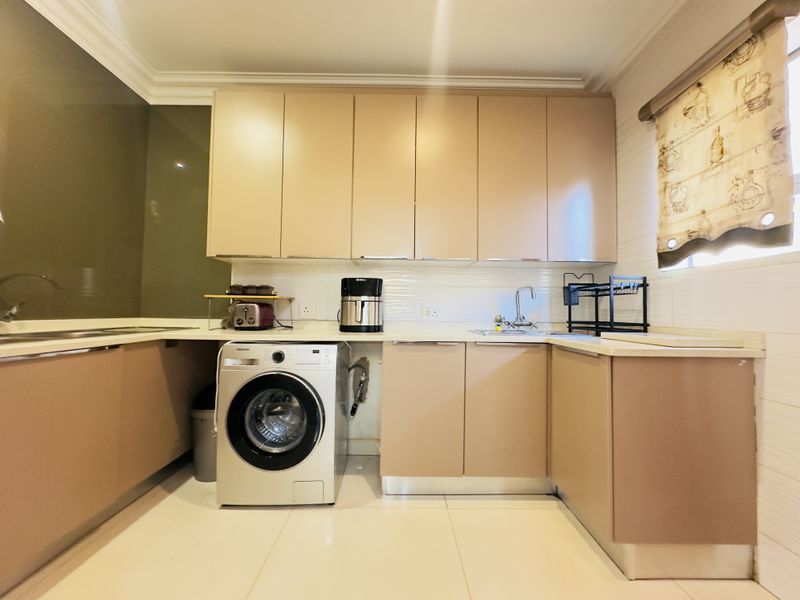 A functional laundry room featuring built-in cabinetry, stone countertops, a stainless steel sink, and tiled flooring.