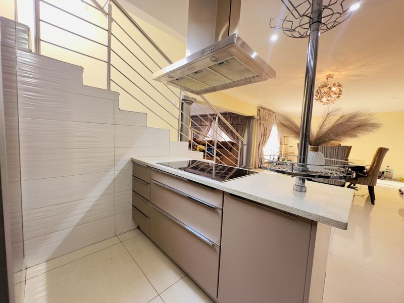 Modern kitchen island featuring a built-in induction hob, stainless steel extractor fan, and stone countertop, positioned adjacent to an open-plan living area and staircase.