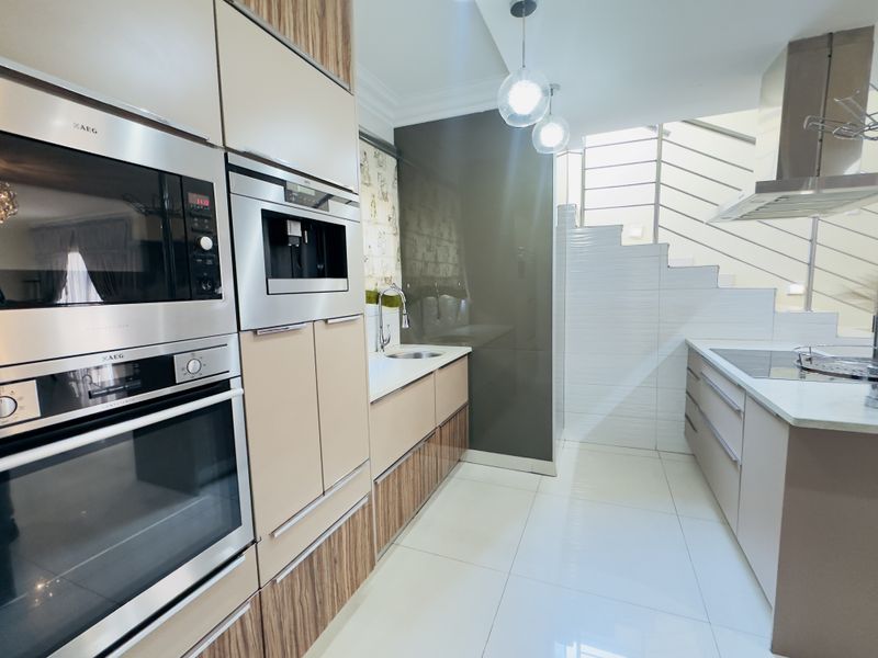 Modern kitchen featuring integrated AEG appliances, sleek cabinetry, tiled flooring, and a contemporary staircase with stainless steel balustrades.