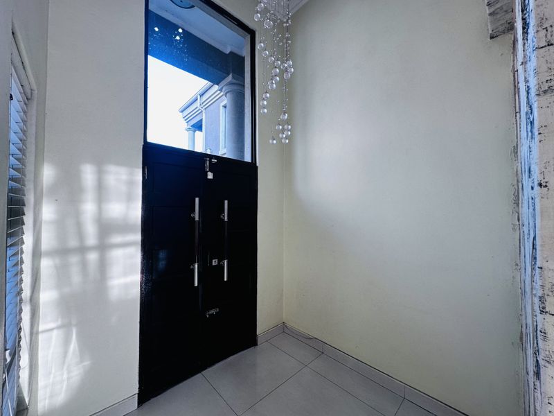 A bright entrance foyer featuring a double front door with a transom window, tiled flooring, and a decorative pendant light fixture.