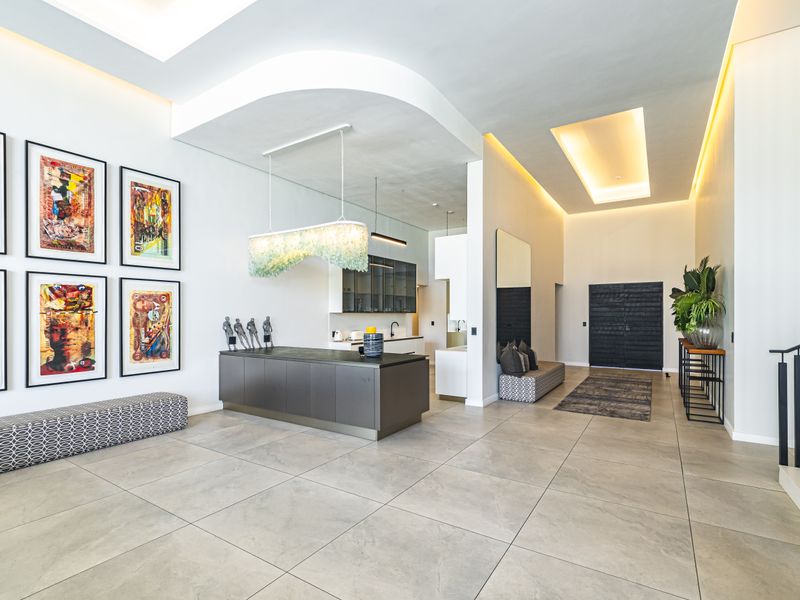 Spacious open-plan living area featuring high ceilings with recessed lighting, large format floor tiles, and a modern kitchen with sleek cabinetry.