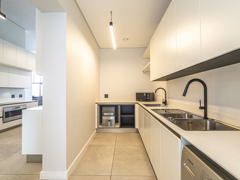 A modern, well-appointed scullery featuring sleek white cabinetry, stone countertops, dual stainless steel sinks, and integrated appliance spaces.