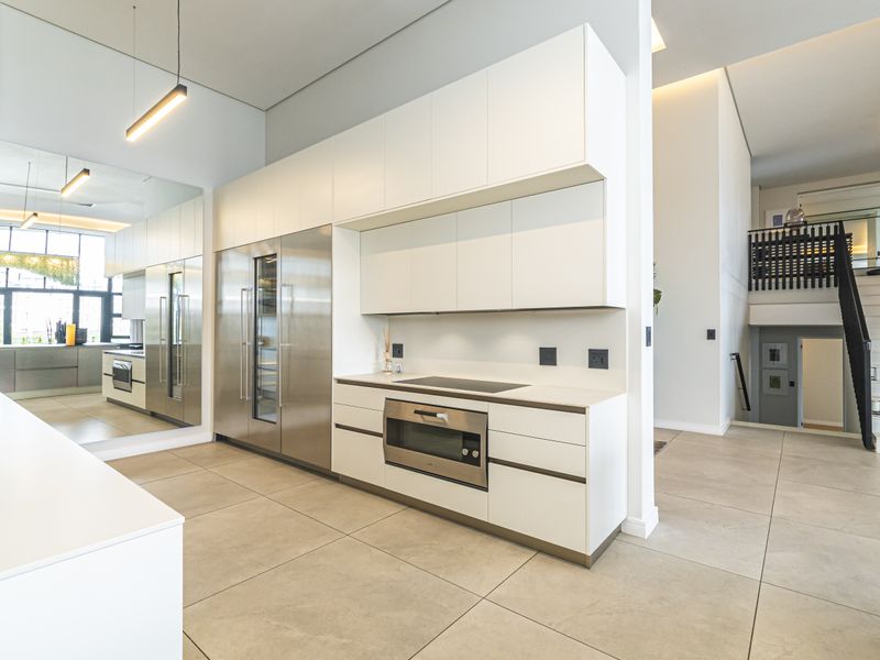 Modern open-plan kitchen featuring sleek white cabinetry, integrated stainless steel appliances, induction hob, built-in oven, and large format floor tiles.
