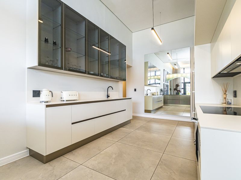 Modern kitchen featuring sleek white cabinetry, glass-fronted upper cabinets, integrated appliances, and large-format floor tiles in a clean, contemporary design.