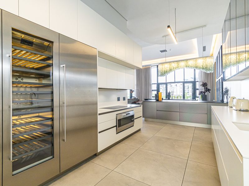 Modern open-plan kitchen featuring high-end integrated stainless steel appliances, sleek white cabinetry, stone countertops, and large format floor tiles.