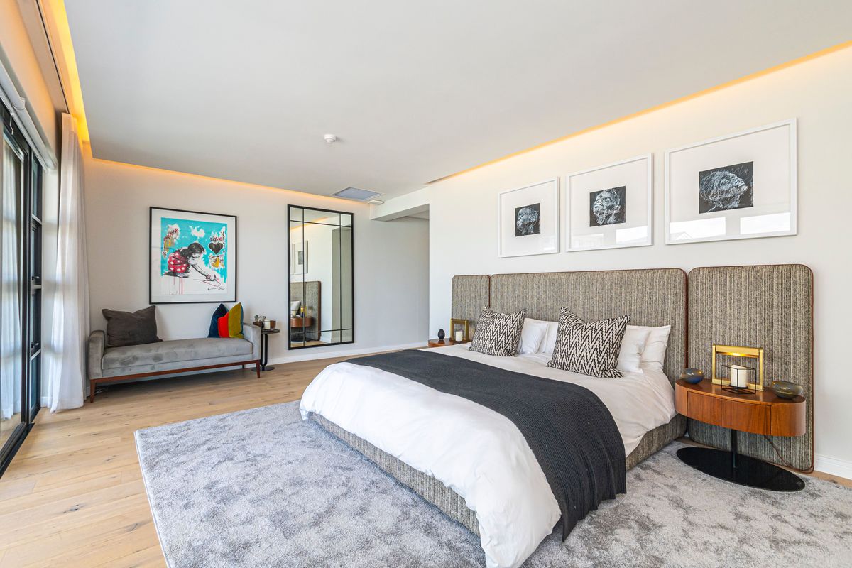 A spacious, modern bedroom featuring light timber flooring, recessed ceiling lighting, and large sliding glass doors leading to an outdoor area.