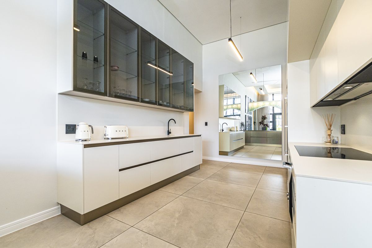 Modern kitchen featuring sleek white cabinetry, glass-fronted upper cabinets, integrated appliances, and large-format floor tiles in a clean, contemporary design.