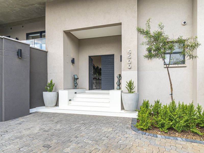 Modern apartment entrance featuring a paved driveway, raised white concrete steps, and a contemporary dark timber front door.