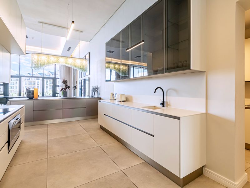 Modern open-plan kitchen featuring sleek handleless cabinetry, stone countertops, integrated appliances, and high-end finishes in a bright, contemporary apartment setting.