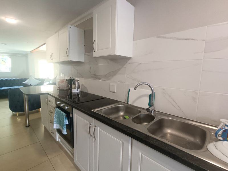 Modern open-plan kitchen featuring white cabinetry, marble-look tiled splashbacks, dark countertops, and integrated stainless steel sink and cooking appliances.