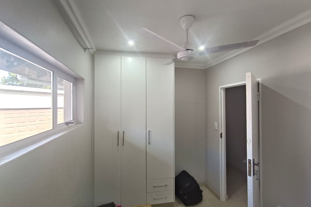 A clean, neutral bedroom featuring built-in white cupboards, a ceiling fan, and tiled flooring, offering a bright and functional space.