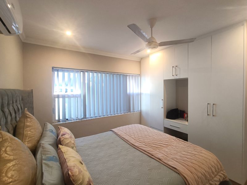 A well-maintained bedroom featuring built-in cupboards, a ceiling fan, vertical blinds, and an air conditioning unit.