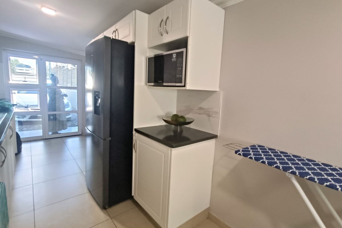 A functional kitchen area featuring white built-in cabinetry, dark stone countertops, a built-in microwave, and tiled flooring with access to an outdoor area.