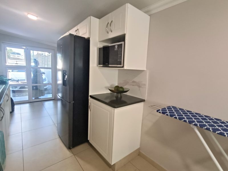 A functional kitchen area featuring white built-in cabinetry, dark stone countertops, a built-in microwave, and tiled flooring with access to an outdoor area.