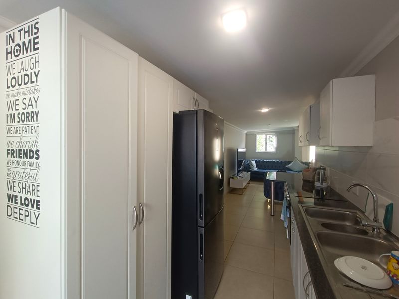 Open plan kitchen and living area featuring modern white cabinetry, tiled flooring, and a functional layout connecting the cooking space to the lounge.