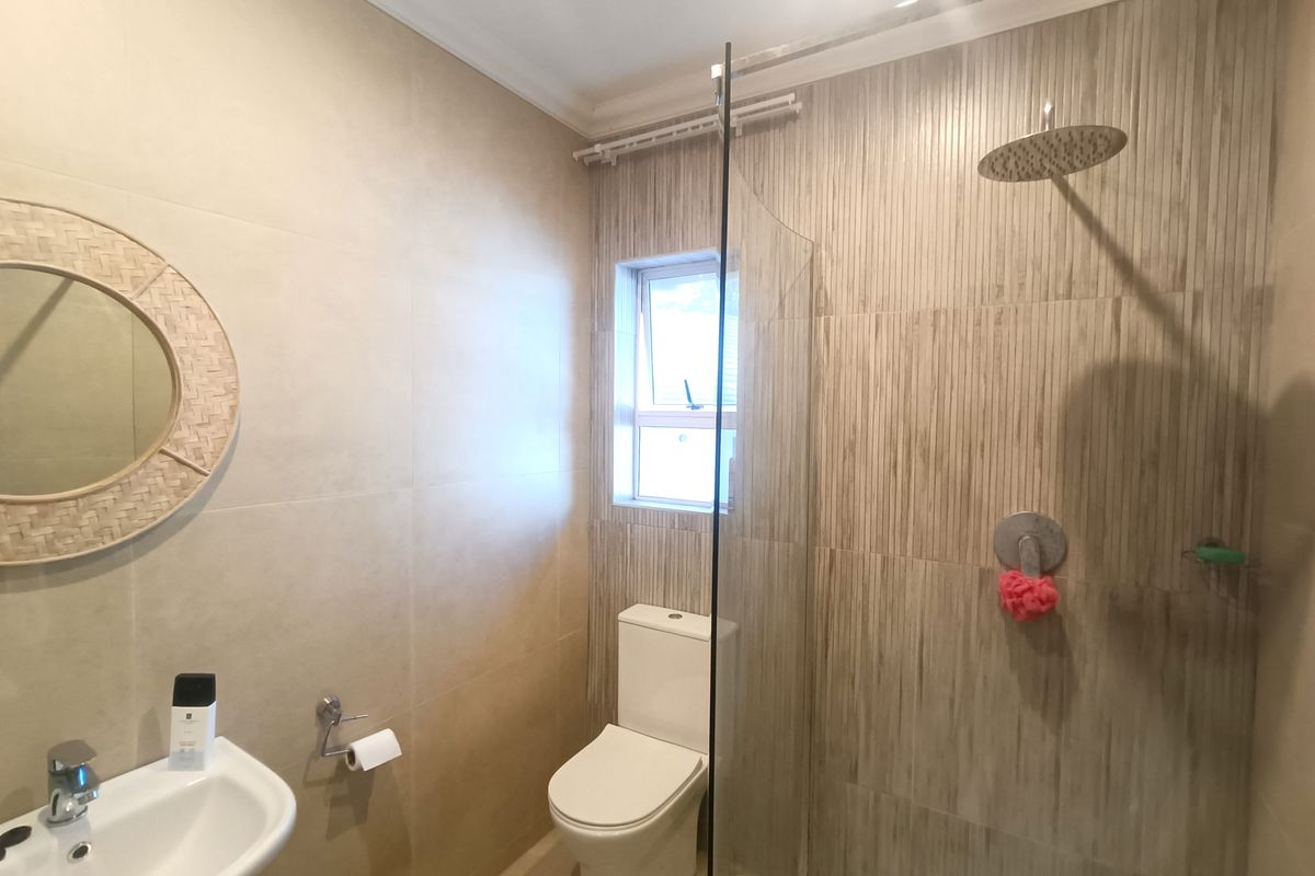 Modern bathroom featuring a glass-enclosed rain shower, wall-mounted basin, and neutral floor-to-ceiling tiling.