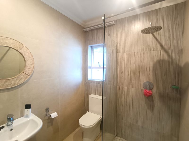 Modern bathroom featuring a glass-enclosed rain shower, wall-mounted basin, and neutral floor-to-ceiling tiling.