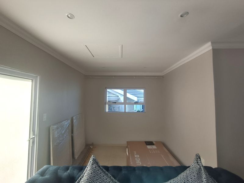 A bright, neutral-toned bedroom featuring tiled flooring, recessed ceiling lighting, and direct access to an outdoor area through a sliding glass door.